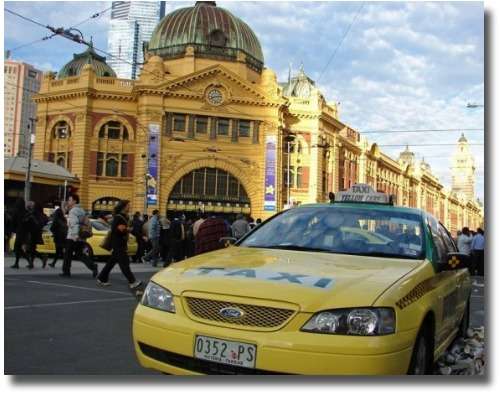 melbourne cab : A yellow taxi parked in front of a large building.