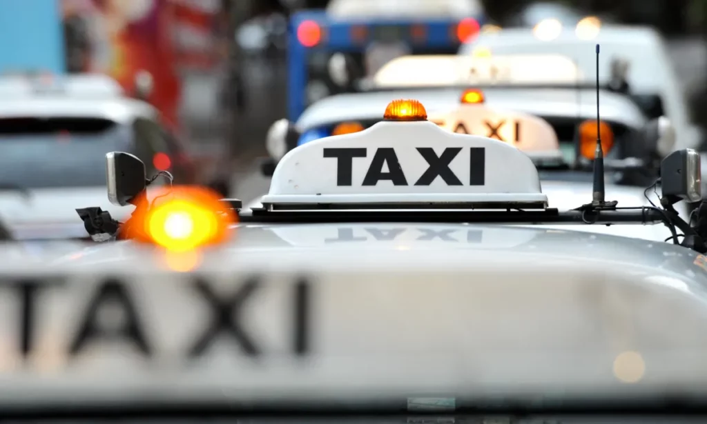 A silver taxi car, equipped with a prominent taxi sign on the front.